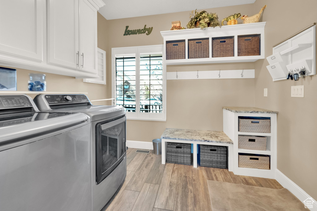 Laundry room featuring cabinet space, baseboards, washer and clothes dryer, and light wood-style flooring