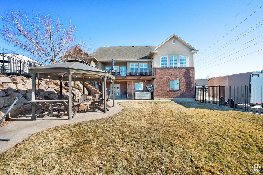 Back of property with a gazebo, brick siding, a patio, and a balcony