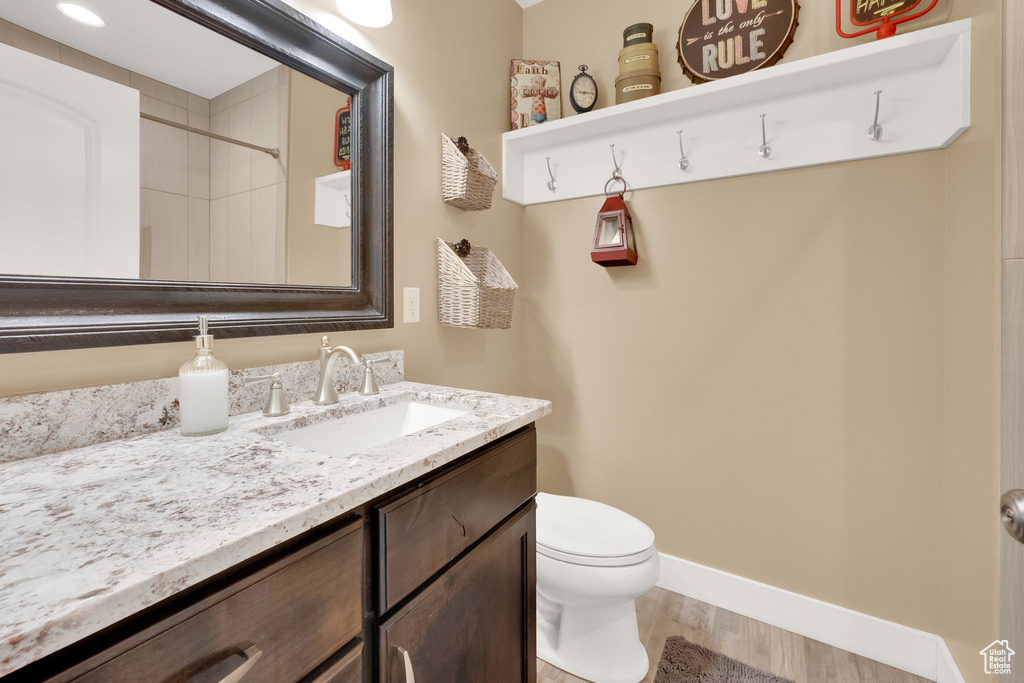 Bathroom with vanity, wood finished floors, toilet, a shower, and baseboards
