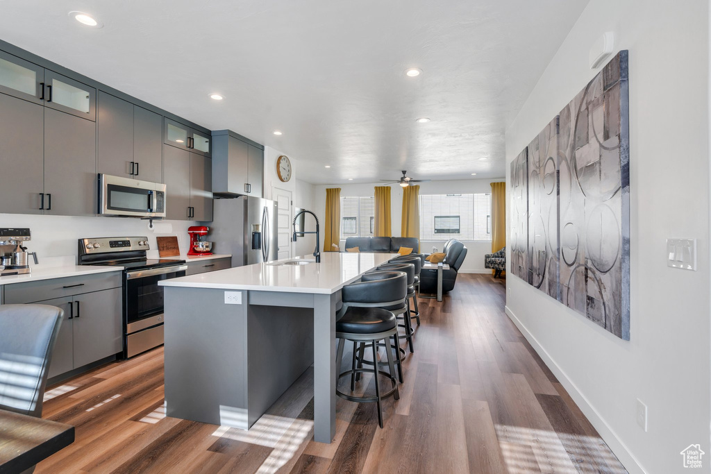 Kitchen featuring appliances with stainless steel finishes, an island with sink, a kitchen bar, wood finished floors, and recessed lighting