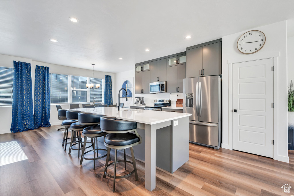 Kitchen with stainless steel appliances, a chandelier, a kitchen island with sink, a kitchen breakfast bar, and light countertops