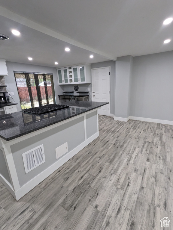 Kitchen featuring white cabinetry, light wood-type flooring, baseboards, recessed lighting, and dark stone countertops