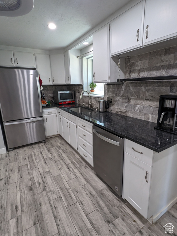 Kitchen with appliances with stainless steel finishes, a sink, backsplash, white cabinetry, and light wood finished floors