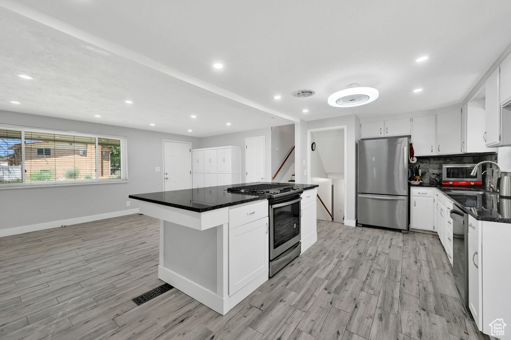 Kitchen with appliances with stainless steel finishes, light wood-style floors, baseboards, white cabinets, and recessed lighting