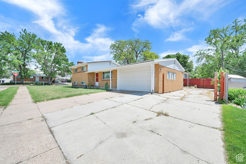 Tri-level home with brick siding, concrete driveway, a garage, and a chimney