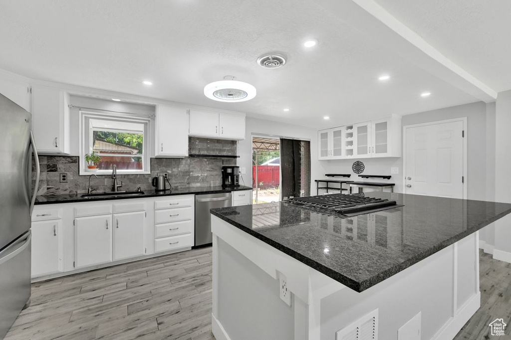 Kitchen with appliances with stainless steel finishes, a sink, light wood-style floors, white cabinets, and tasteful backsplash