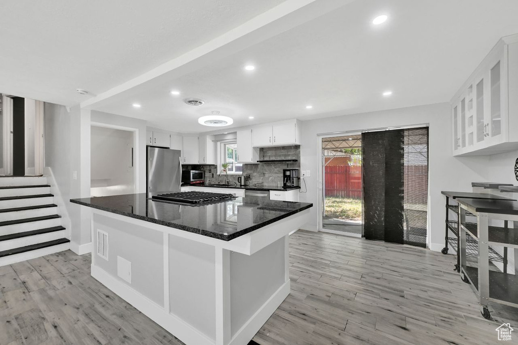 Kitchen featuring stainless steel appliances, white cabinets, light wood-style floors, decorative backsplash, and recessed lighting