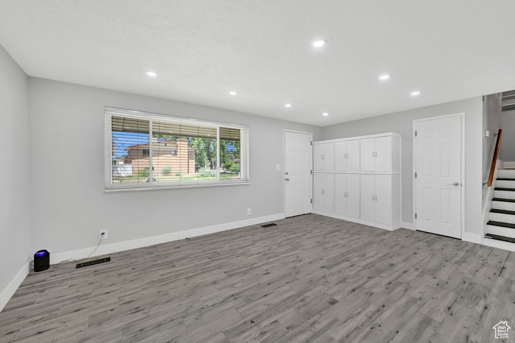Unfurnished living room with recessed lighting, wood finished floors, baseboards, and stairway