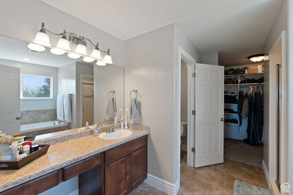 Bathroom with a garden tub, a spacious closet, toilet, vanity, and baseboards