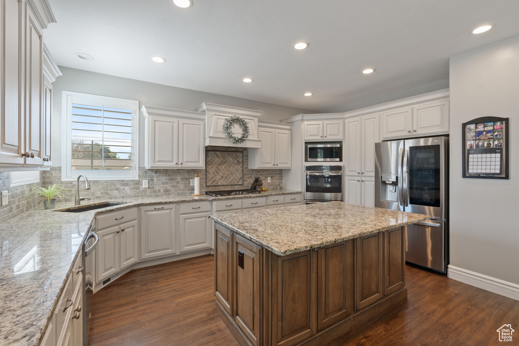 Kitchen with stainless steel appliances, a sink, a center island, white cabinetry, and tasteful backsplash