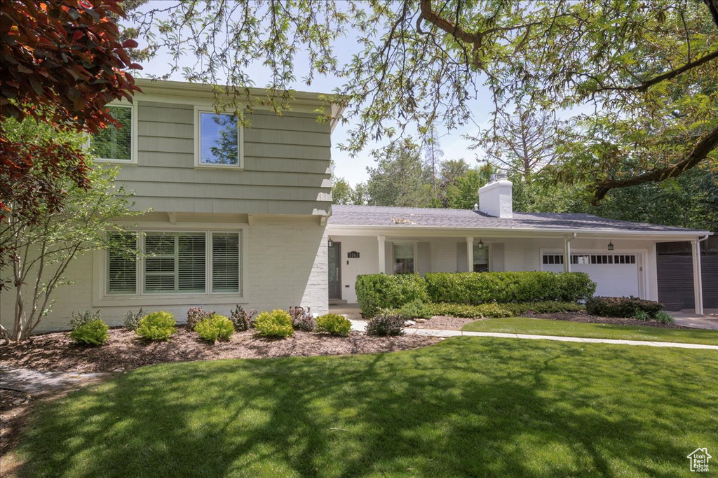 View of front of property with a front yard, an attached garage, a chimney, and brick siding