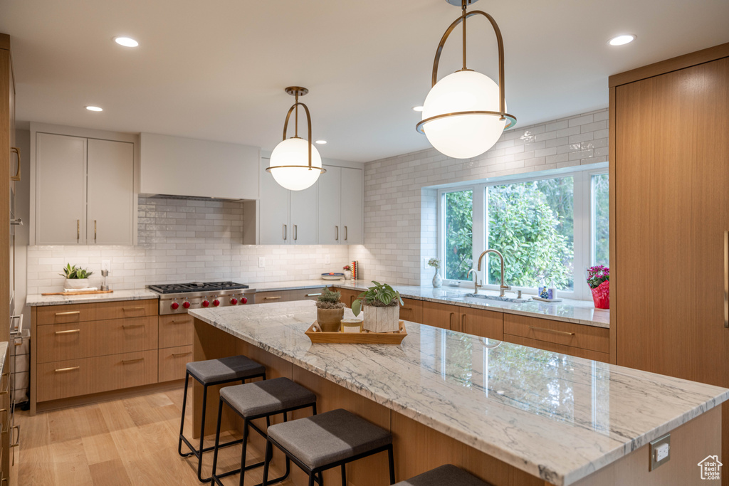 Kitchen with white cabinetry, sink, hanging light fixtures, stainless steel gas cooktop, and light stone countertops
