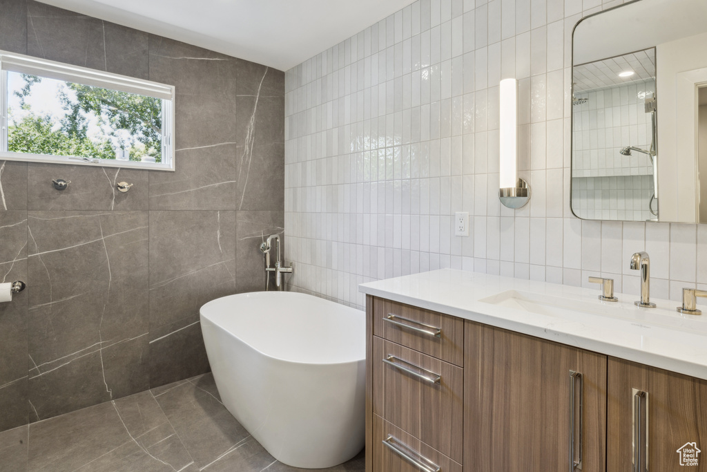 Full bath with tile walls, vanity, and a soaking tub