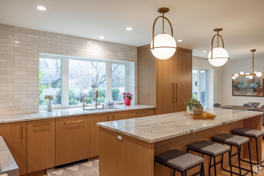 Kitchen with hanging light fixtures, light stone countertops, sink, and a center island