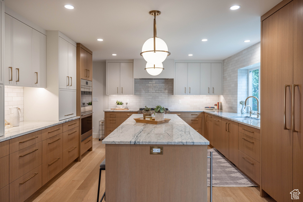 Kitchen with white cabinetry, a center island, sink, and hanging light fixtures