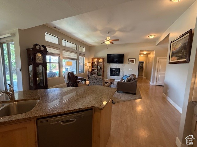 Kitchen with dishwashing machine, a sink, light wood finished floors, ceiling fan, and a glass covered fireplace