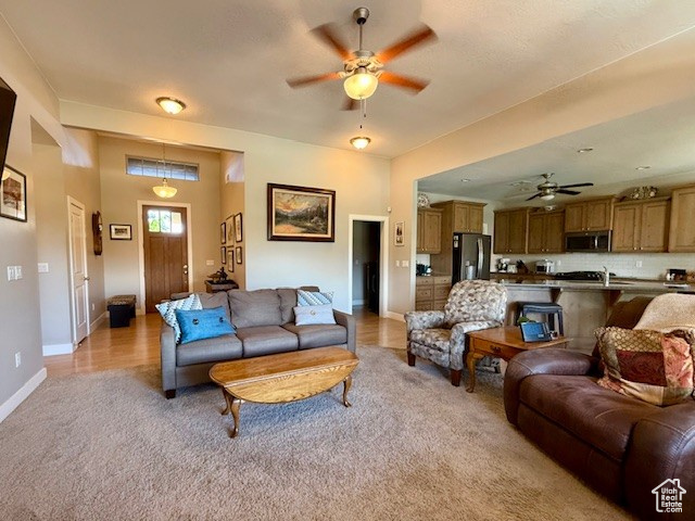 Living area with ceiling fan, light carpet, and baseboards