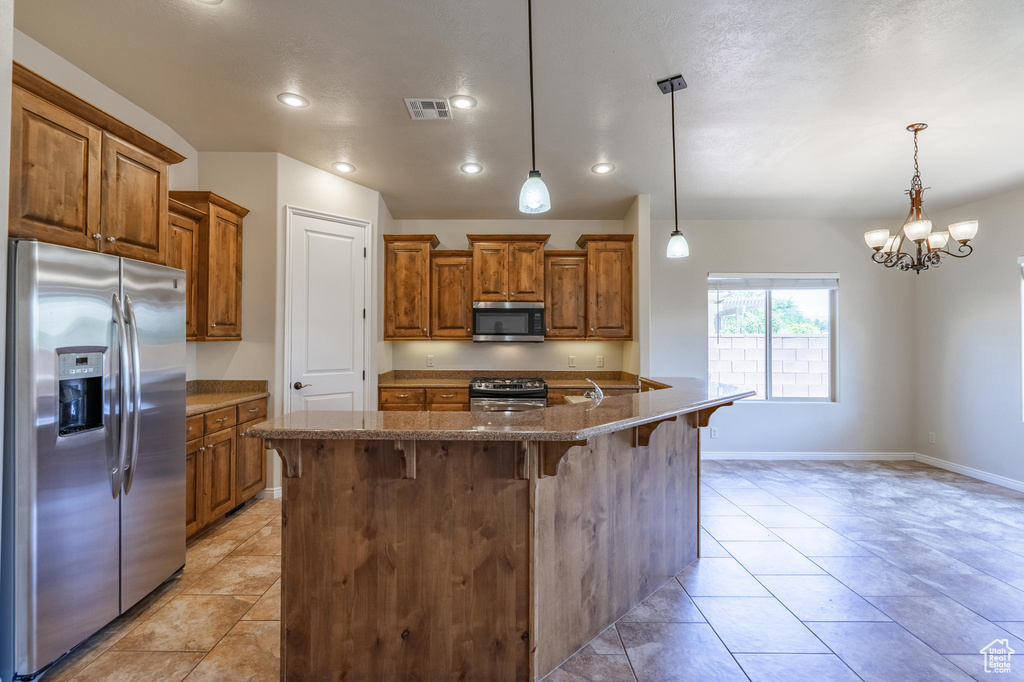 Kitchen featuring appliances with stainless steel finishes, brown cabinets, a breakfast bar, pendant lighting, and a chandelier