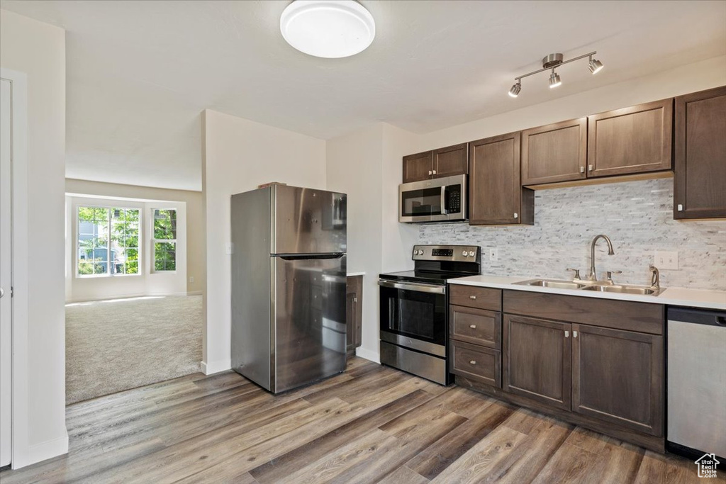 Kitchen featuring stainless steel appliances, a sink, light wood finished floors, and backsplash