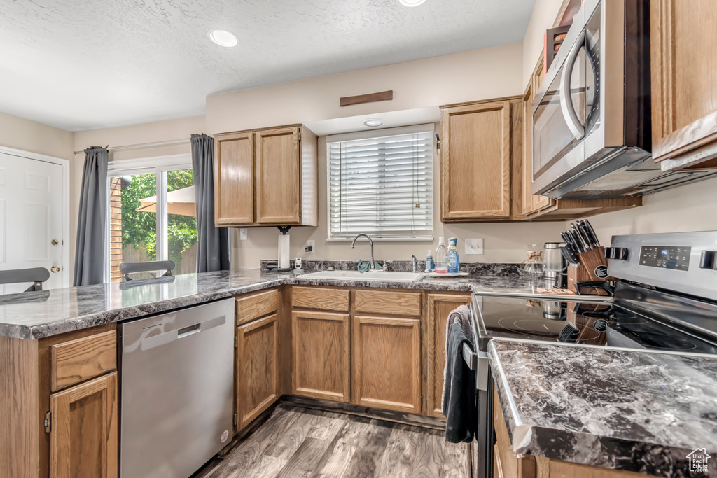 Kitchen with stainless steel appliances, a sink, a peninsula, light wood finished floors, and a textured ceiling