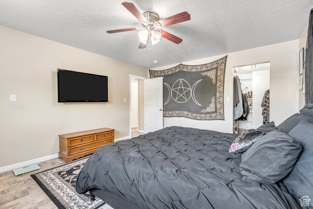 Bedroom with a textured ceiling, baseboards, a walk in closet, light stone finish flooring, and a ceiling fan