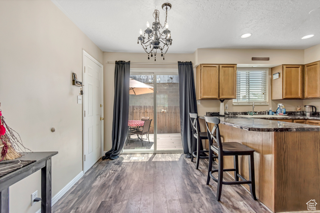 Kitchen with a textured ceiling, a chandelier, dark wood-type flooring, baseboards, and a kitchen bar