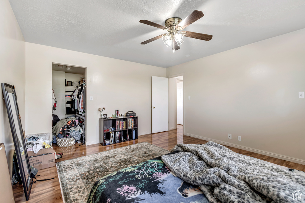 Bedroom with a spacious closet, wood finished floors, ceiling fan, and baseboards