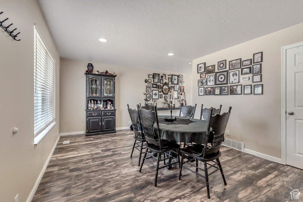 Dining space featuring dark wood-style flooring, baseboards, recessed lighting, a textured ceiling, and a bar