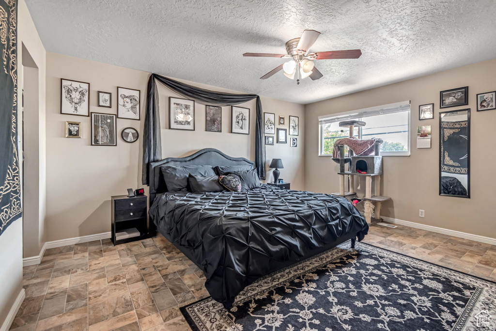 Bedroom with stone finish floors, a textured ceiling, baseboards, and ceiling fan