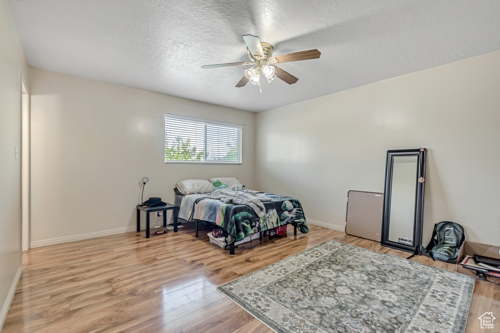 Bedroom featuring light wood finished floors, a textured ceiling, baseboards, and a ceiling fan