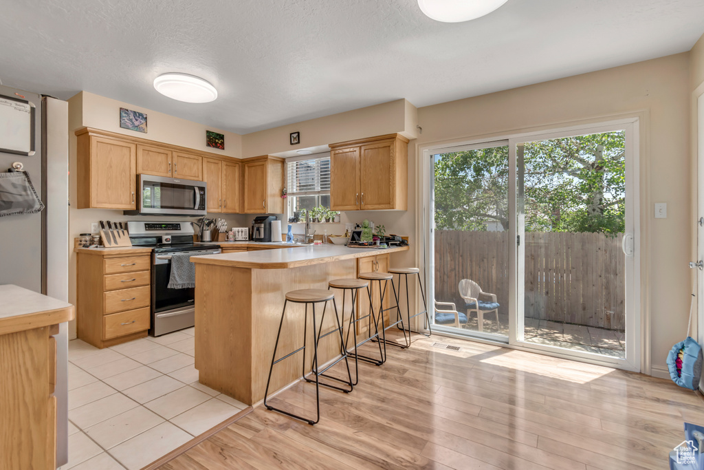 Kitchen featuring stainless steel appliances, light countertops, a kitchen bar, a peninsula, and light wood-type flooring