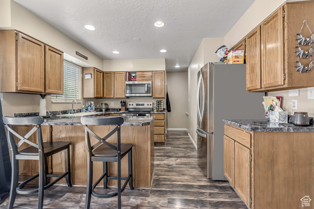 Kitchen with appliances with stainless steel finishes, a peninsula, a textured ceiling, a breakfast bar area, and a sink