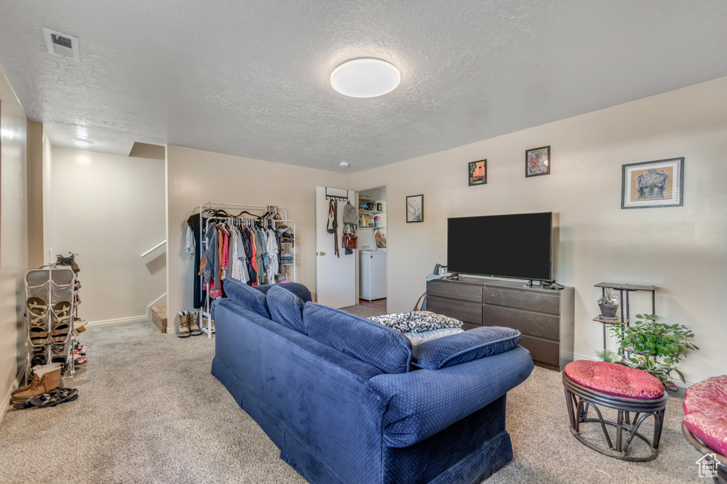 Carpeted living area featuring a textured ceiling, baseboards, washer / dryer, and stairway