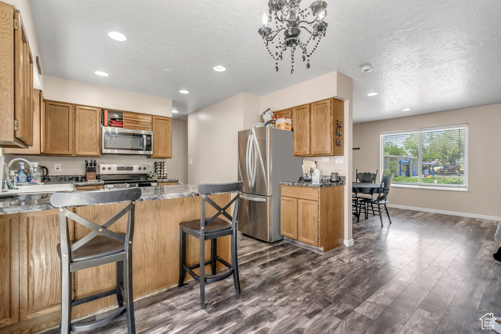 Kitchen with appliances with stainless steel finishes, recessed lighting, a kitchen breakfast bar, dark wood-style flooring, and a textured ceiling