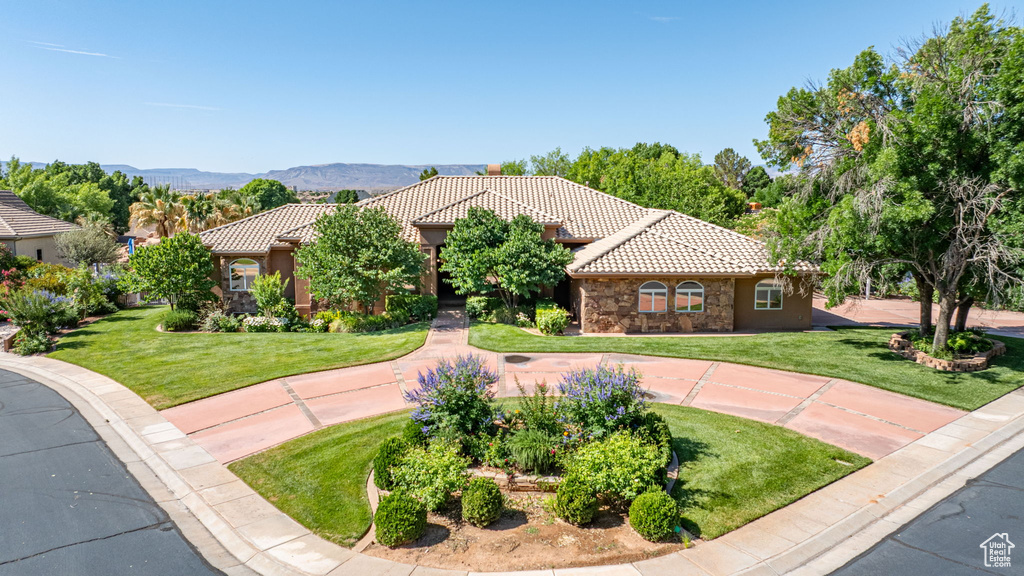 Mediterranean / spanish-style home featuring a tile roof, a front lawn, stone siding, and a mountain view