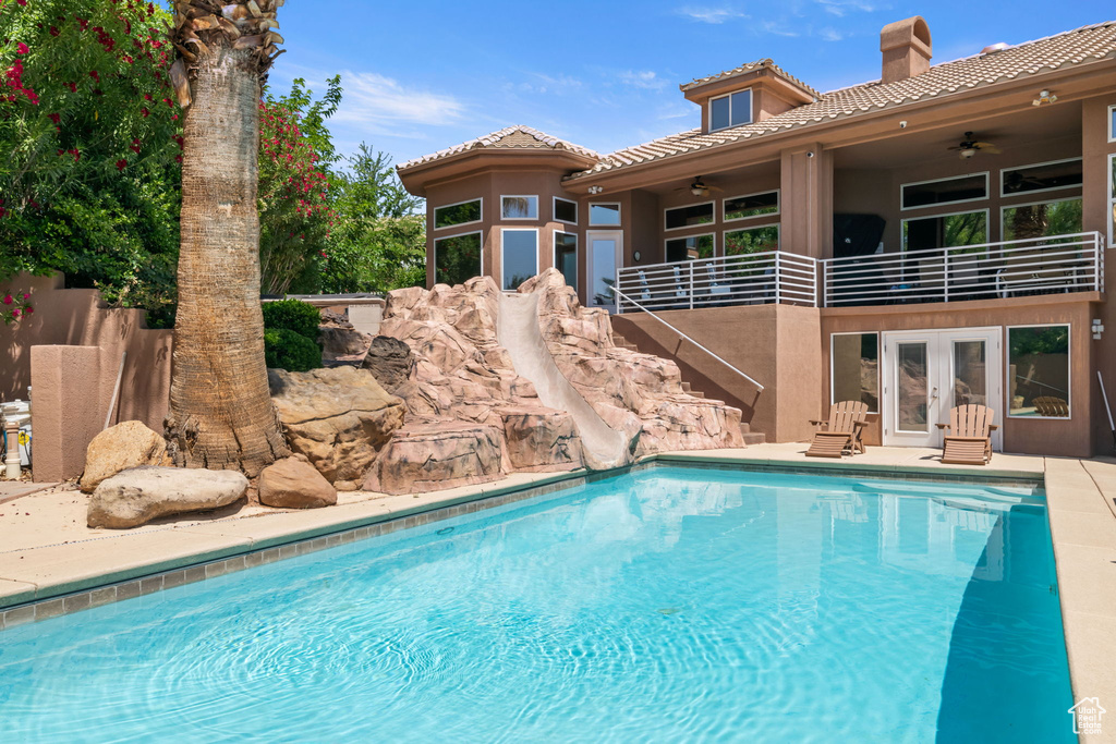 Swimming pool with ceiling fan, a water slide, french doors, and stairs