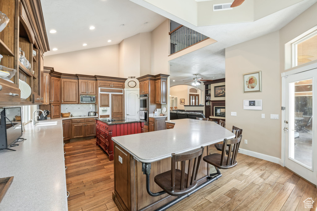 Kitchen featuring a ceiling fan, built in appliances, high vaulted ceiling, a center island, and wood finished floors