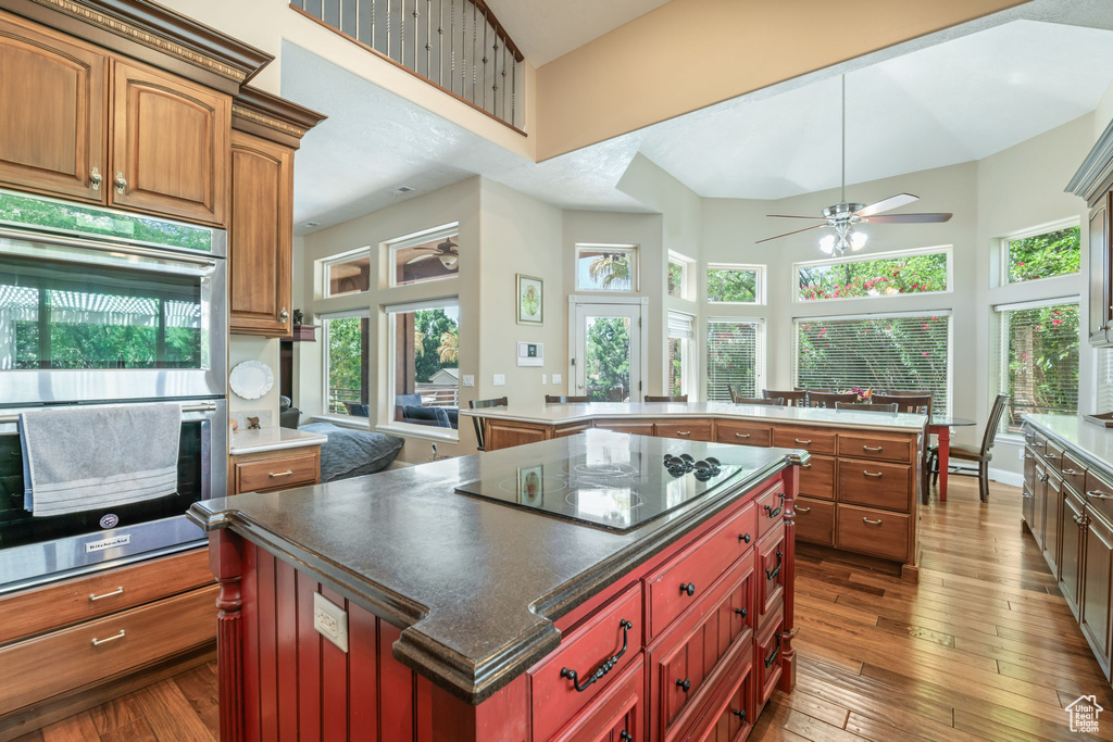 Kitchen featuring black electric cooktop, a large island, double oven, a ceiling fan, and a towering ceiling