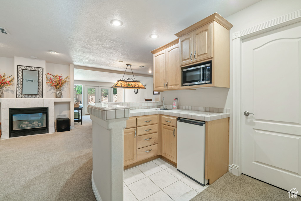 Kitchen featuring light brown cabinets, stainless steel microwave, open floor plan, dishwasher, and tile counters