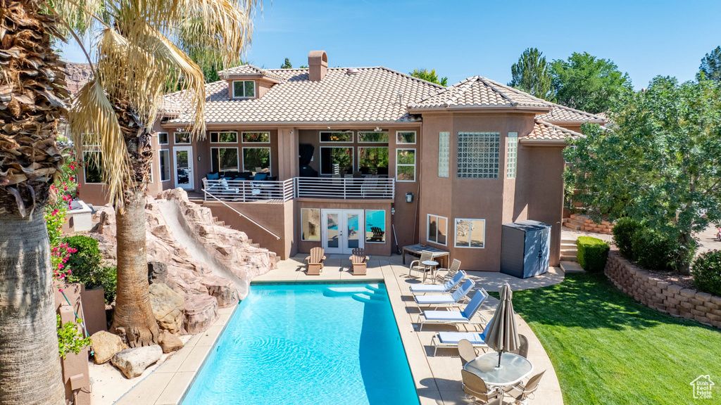 Back of property featuring a tile roof, french doors, stucco siding, an outdoor pool, and a balcony