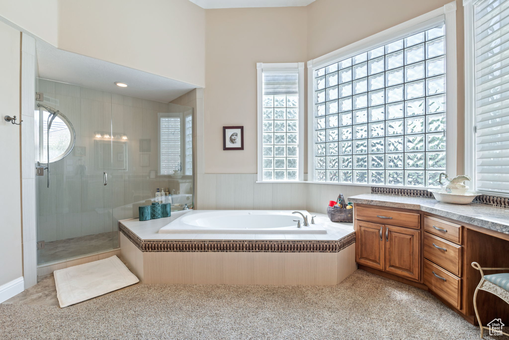 Bathroom featuring healthy amount of natural light, a shower stall, a garden tub, vanity, and a wainscoted wall