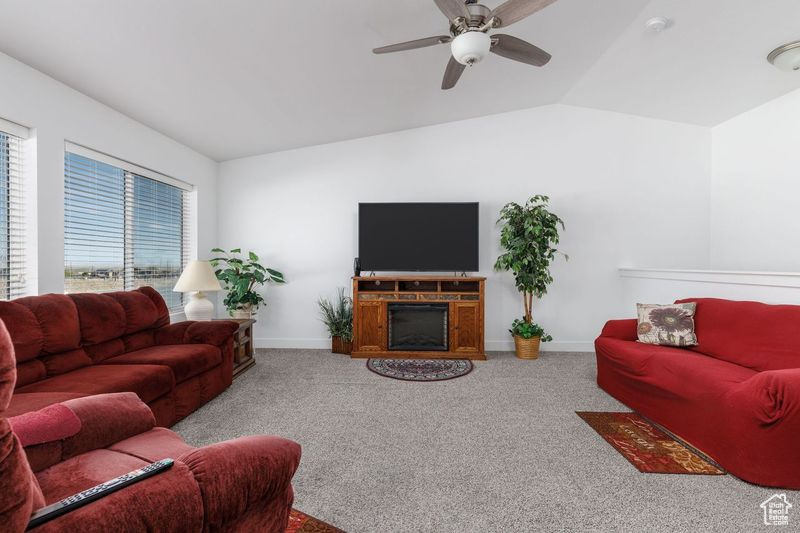 Living room with carpet floors, lofted ceiling, a ceiling fan, and baseboards