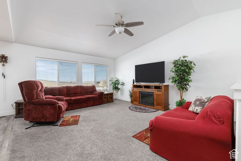 Living room with vaulted ceiling, a fireplace, ceiling fan, and baseboards