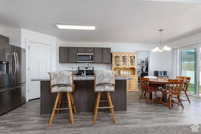 Kitchen featuring stainless steel appliances, wood finished floors, a breakfast bar area, and a kitchen island with sink