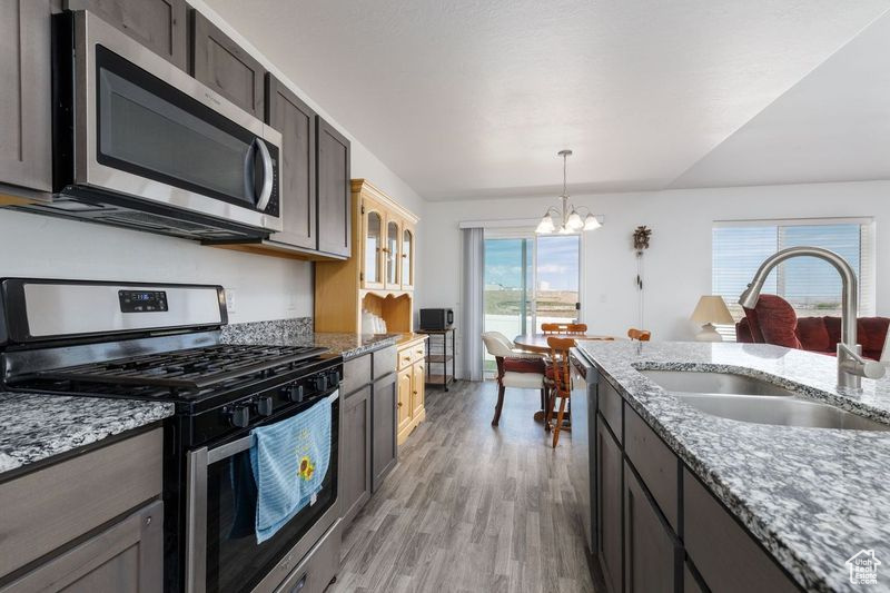 Kitchen featuring appliances with stainless steel finishes, a sink, a chandelier, light wood-type flooring, and hanging light fixtures