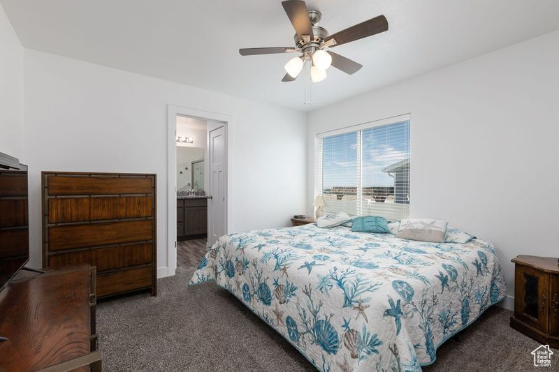 Bedroom with carpet flooring, a ceiling fan, ensuite bath, and baseboards