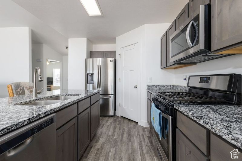Kitchen featuring stainless steel appliances, a sink, light wood-style flooring, light stone counters, and ceiling fan