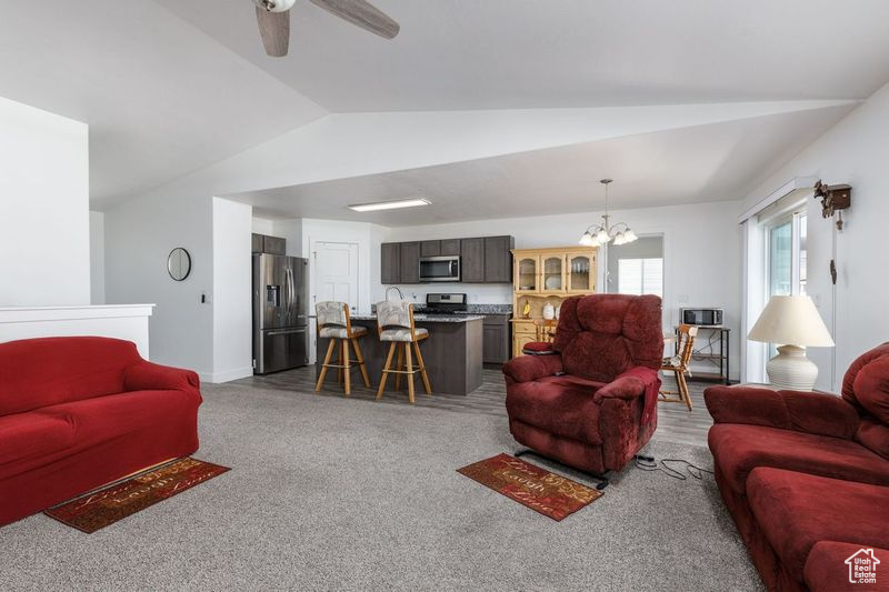 Living room with vaulted ceiling, a chandelier, ceiling fan, carpet flooring, and baseboards