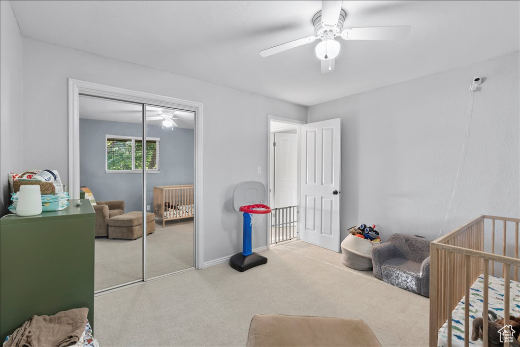 Carpeted bedroom with a closet, a nursery area, ceiling fan, and baseboards