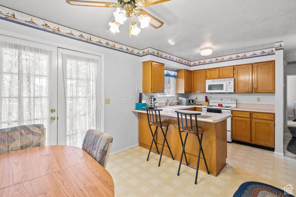 Kitchen with white appliances, light flooring, brown cabinets, ceiling fan, and light countertops